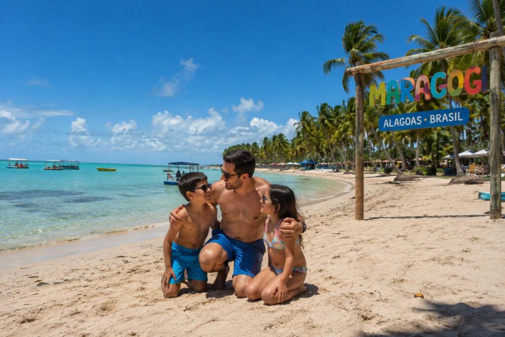 Família brincando em praia de água calma e clara no Brasil, em Maragogi.